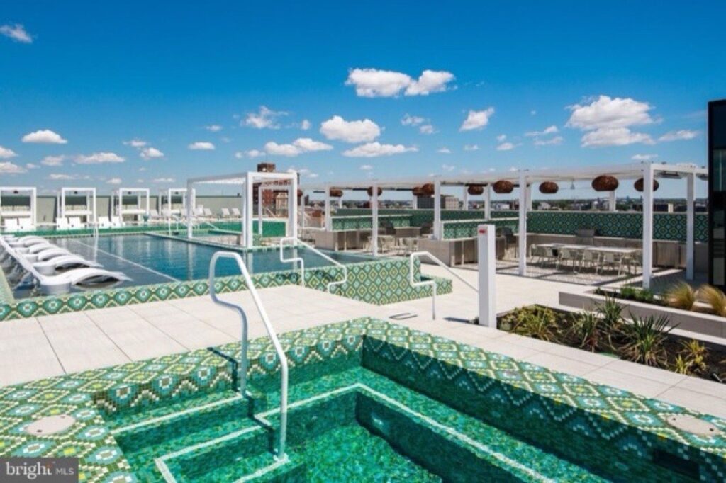 Rooftop pool club with green-tiled hot tubs, cabana lounge seating and Philadelphia skyline views at The Poplar